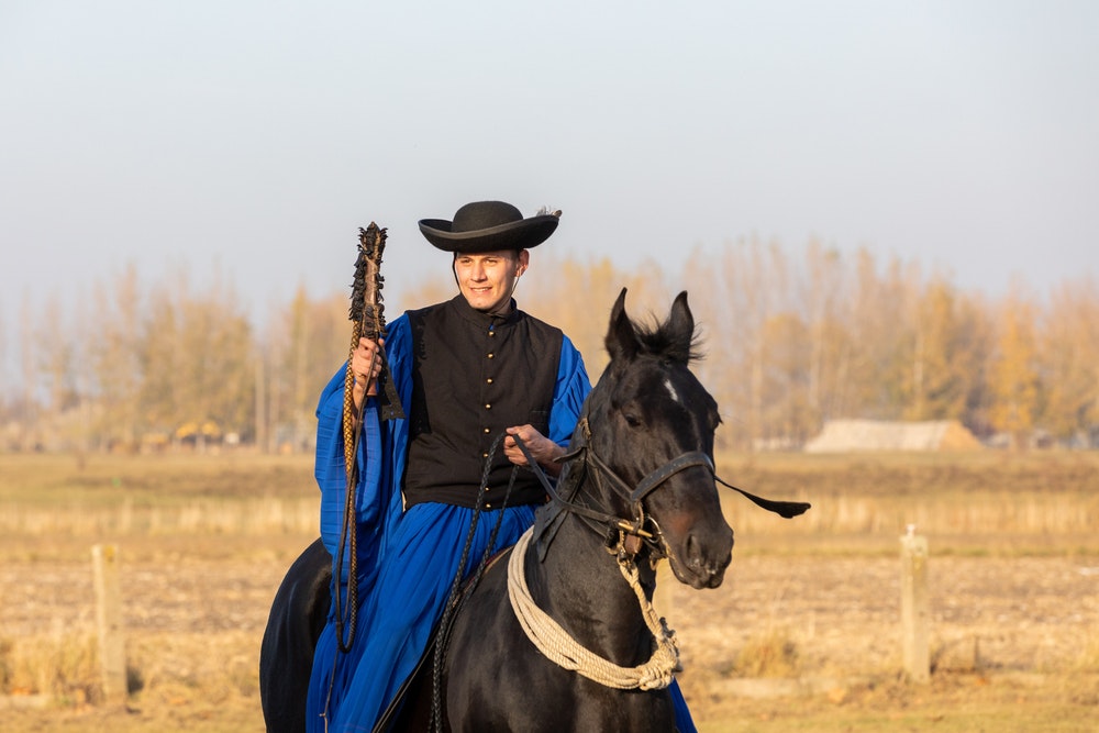 Een Hongaarse tsikos in traditionele klederdracht pronkt met zijn getrainde paard. 