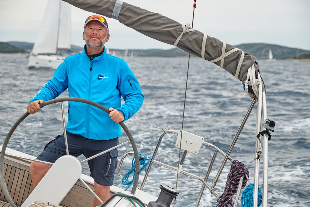 Croatia, Adriatic Sea, 19 September 2019: The brutal captain of the boat is at a steering wheel, jacket of blue color, sailboat compete in a sail regatta, cloudy weather