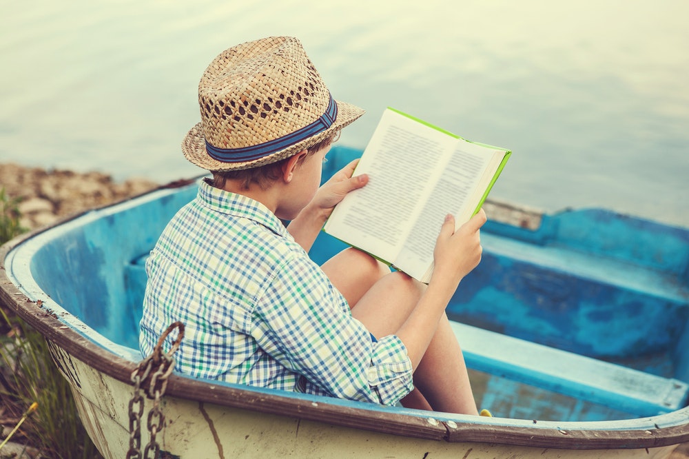 Chlapec s klobúkom na hlave si číta v malej loďke