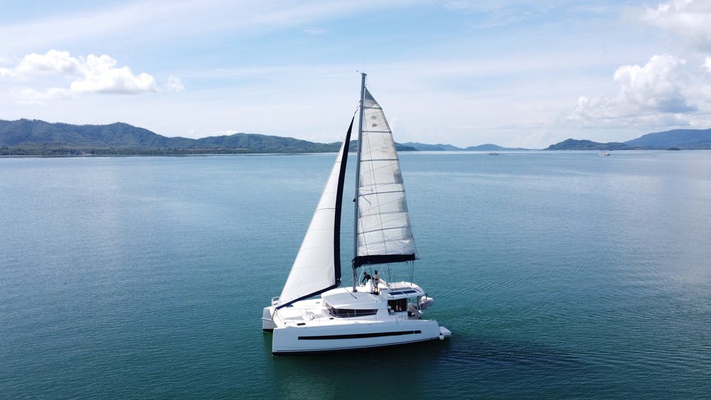 Catamarán de vela con velas abiertas. Catamarán de vela en medio del mar en un paisaje tropical. Catamarán de vela con velas abiertas