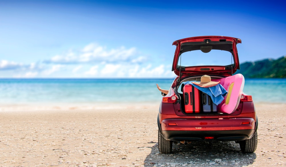Letní čas a červené auto na pláži s několika kufry.