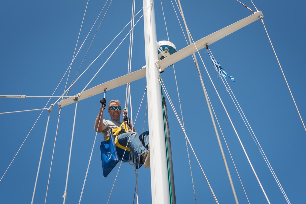 Caucasian male wearing sunglasses, climbing a ship's mast while smiling