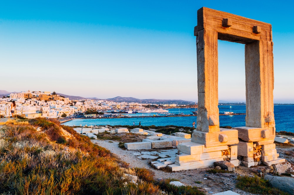 Портара, вратата на хълма на остров Палатия, митичната порта на бог Аполон, на заден план със залива и яхтите.