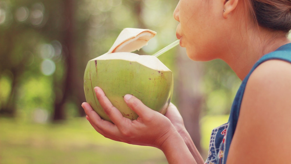 Dekle pije kokosovo vodo naravnost iz kokosa