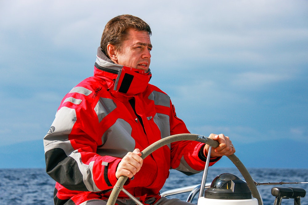 Um marinheiro de casaco desportivo ao leme de um veleiro de regata