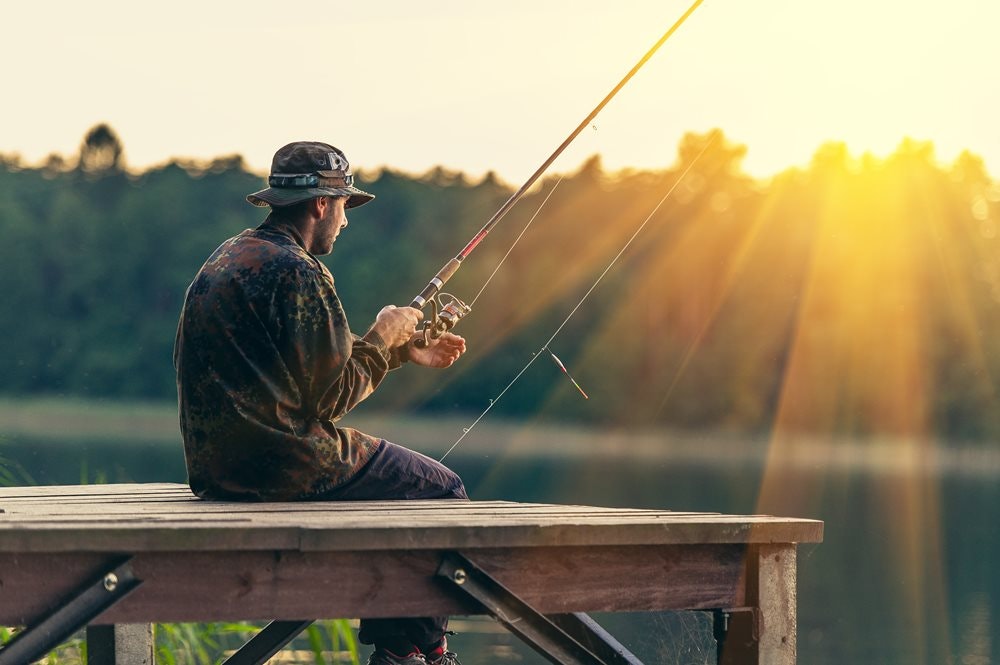 Рибалка сидить на дерев'яному пірсі в капелюсі на заході сонця