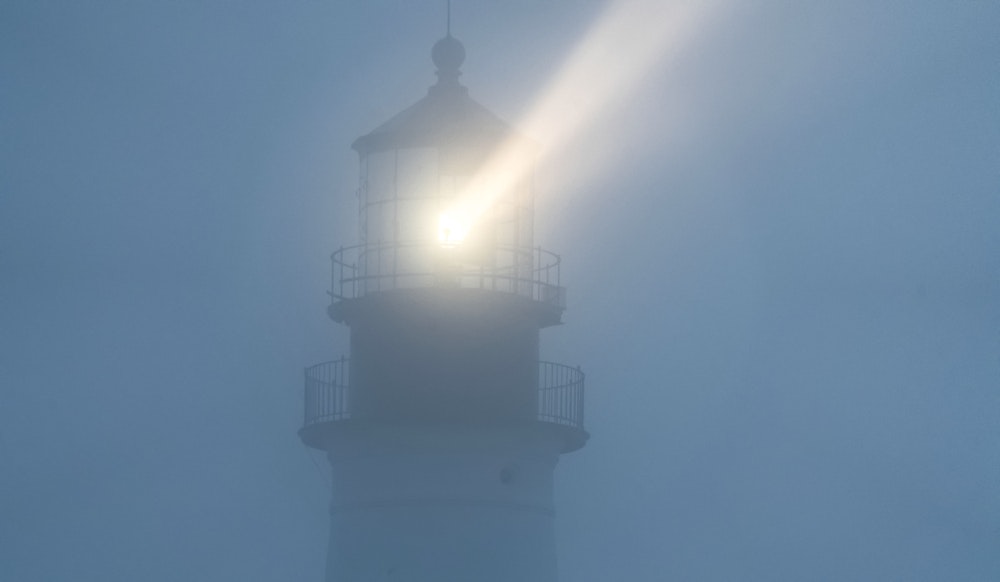 Промені світла від маяка відбиваються в тумані в темряві.