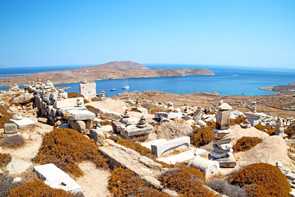 Arkeologisk monument på øya Delos i bakgrunnen med en bukt og en yacht.