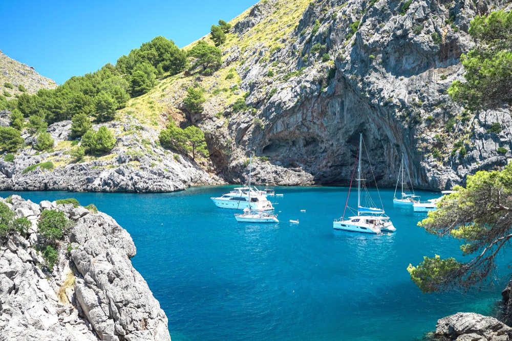 Segelboote und Segelschiffe in einer türkisfarbenen Bucht an den Felsen auf der Insel Mallorca