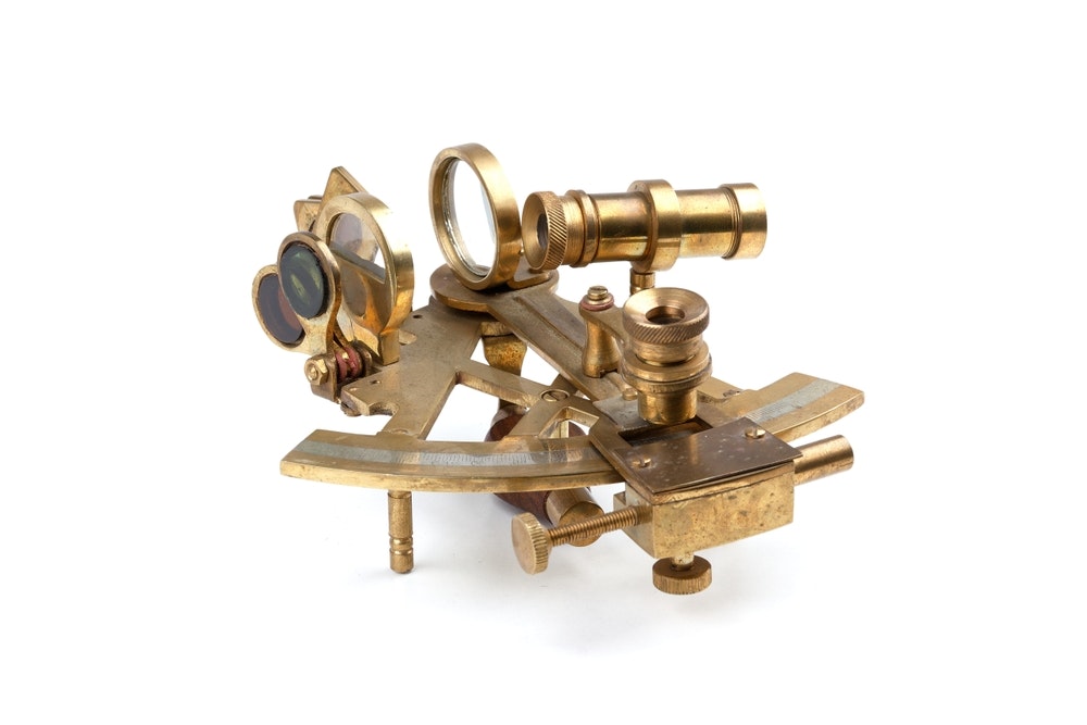 gammal marin sextant med optik mot vit bakgrund