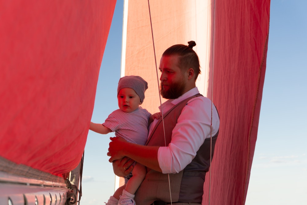 Ένας άντρας κρατά ένα παιδί στην αγκαλιά του σε ένα πλοίο.