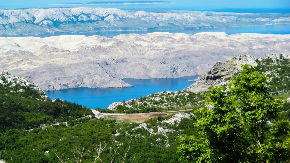 Pohled z pohoří Velebit na zelený les a Středozemní moře na bílých vyprahlých ostrovech Pag, Chorvatsko.