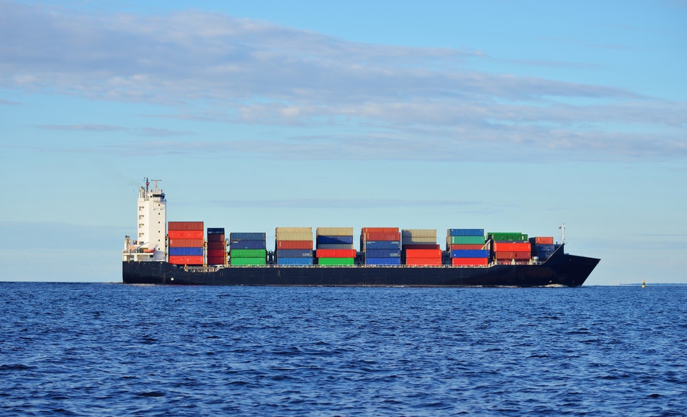 Ein schwarzes Containerschiff, das in ruhigem Wasser in der Nähe des Hafens von Riga fährt