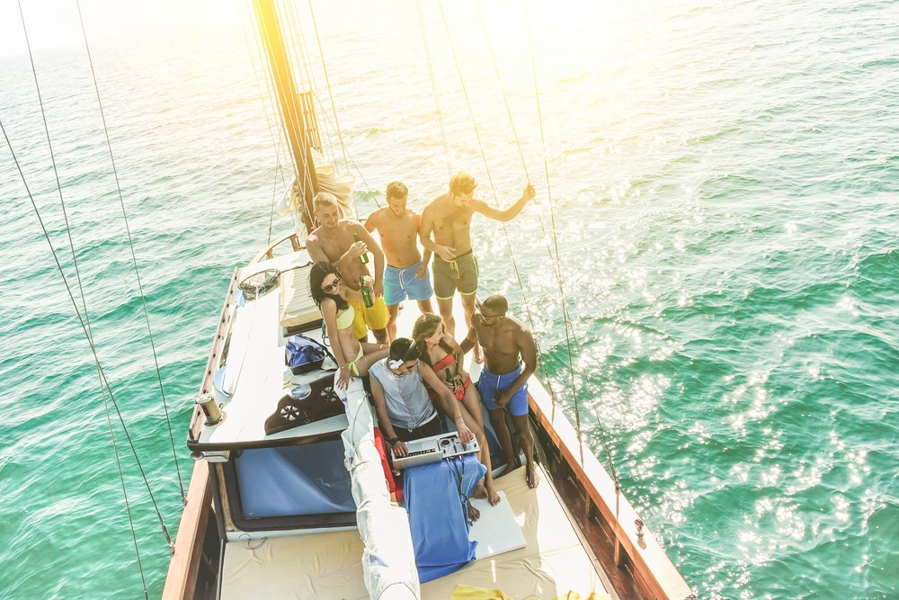 Eine Gruppe junger Leute, die auf einer Party auf einem Segelboot trinken und tanzen, während ein DJ Musik spielt