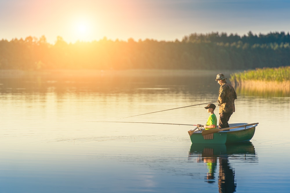 баща и син ловят риба от лодка по залез слънце