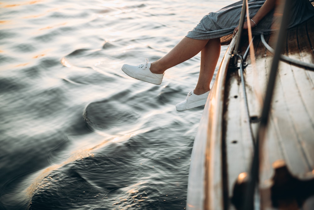 Ноги дівчини в білих кросівках, сидячи на яхті, насолоджуючись заходом сонця