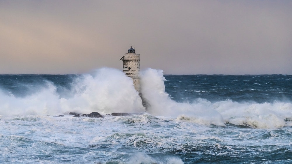 El faro de Mangiabarche con grandes olas chocando contra él en una tormenta.