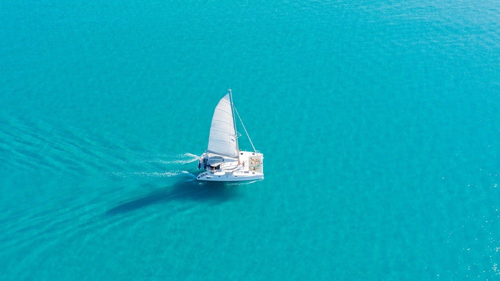 Ein Katamaran segelt auf türkisfarbenem Wasser.