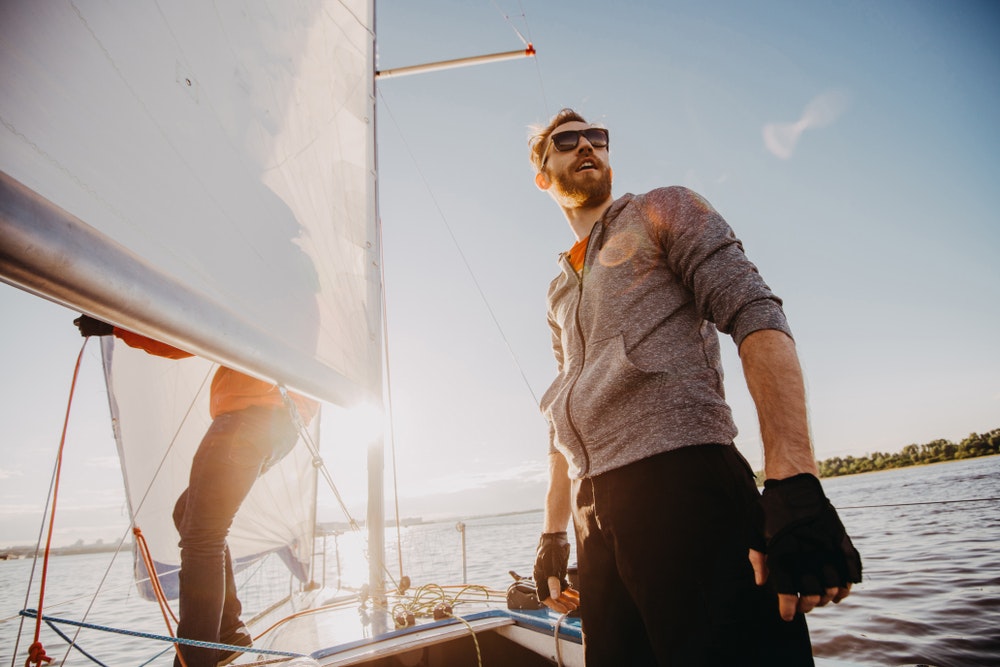 Νέος ναύτης που φορά γυαλιά ηλίου και γάντια σε ένα ιστιοφόρο στο ηλιοβασίλεμα.