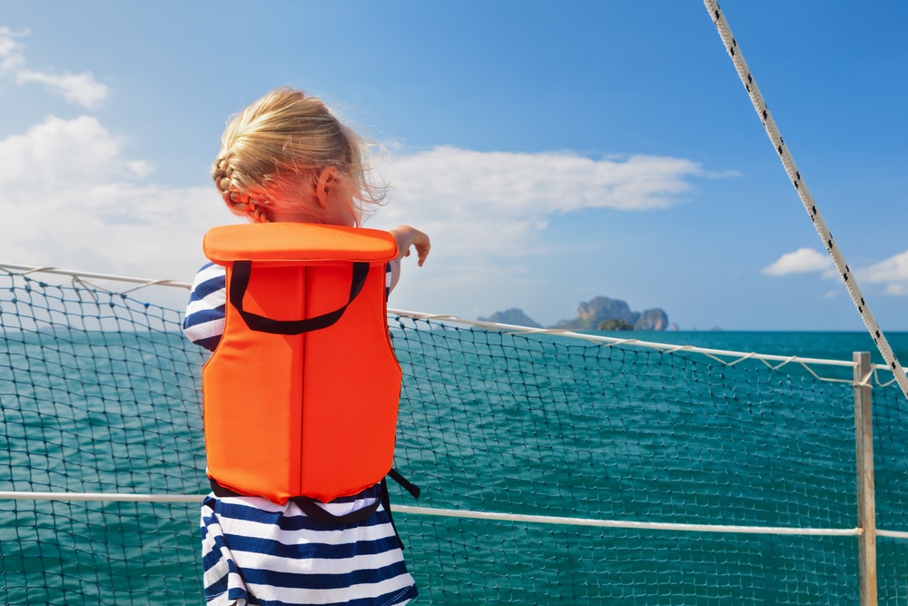 Ein Kind in einer Schwimmweste auf dem Deck eines Schiffes in der Nähe des Sicherheitsnetzes.