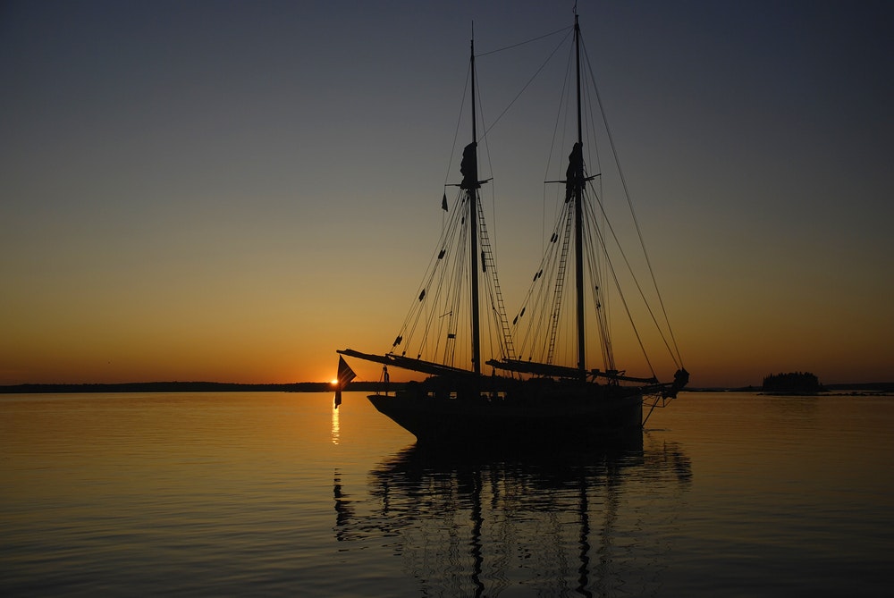 Silhouette of a two-masted schooner against a beautiful sunset with the sun on the horizon.