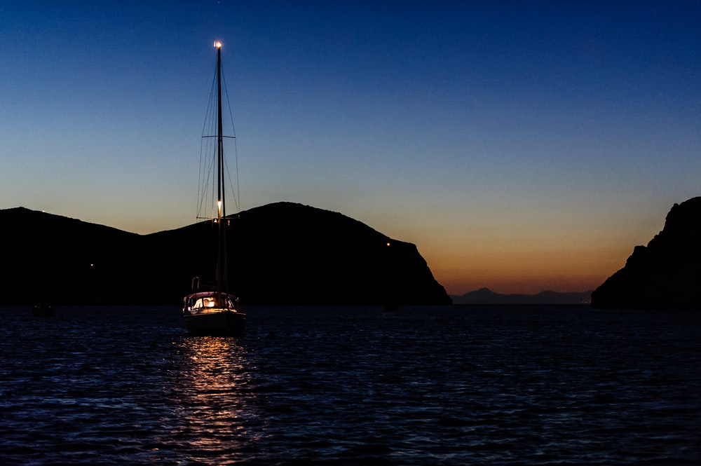 Naktī līcī pietauvota laiva ar ieslēgtu enkura gaismu.