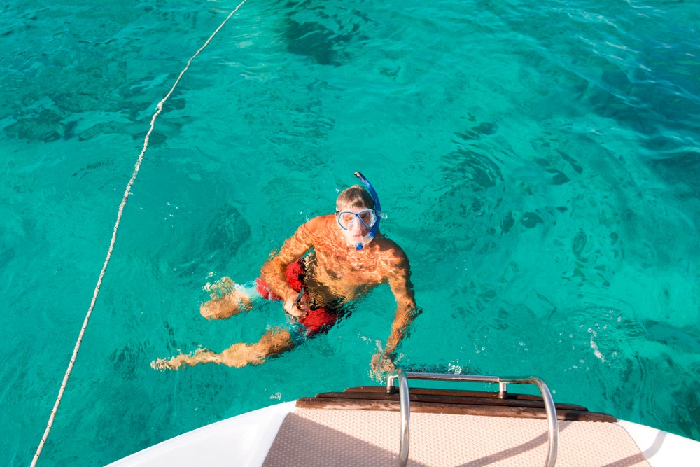 Een man in het water aan de achtersteven van een boot met een snorkel en een duikbril. 