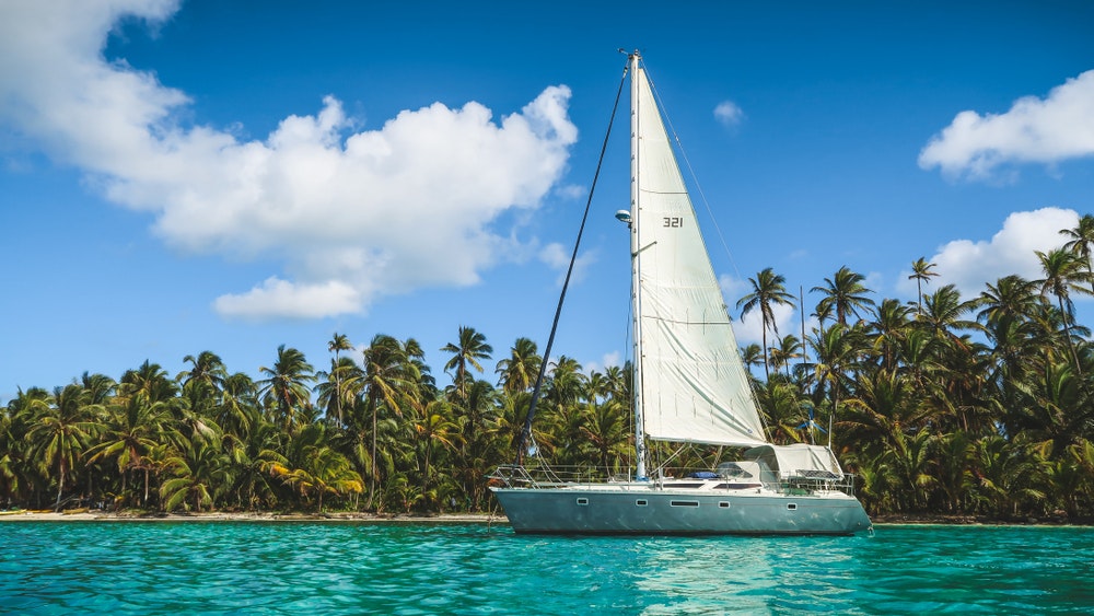 A sailboat anchored in turquoise water in front of the paradise islands of San Blas, Panama