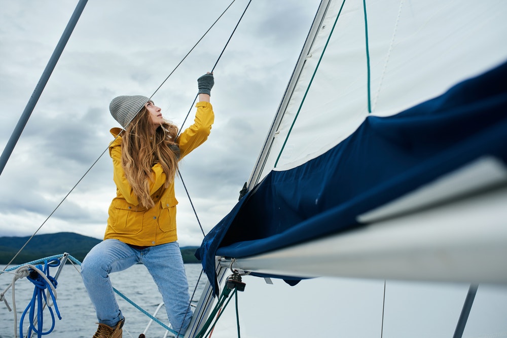 Een jonge vrouw in een gele jas en pet houdt een touw vast op een boot