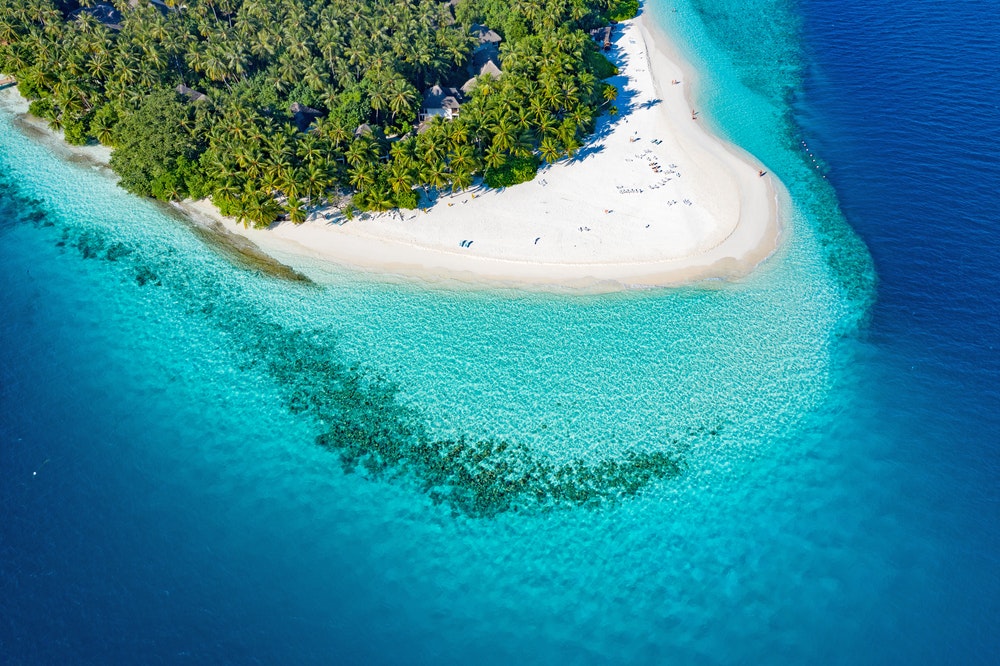 Die Insel der Malediven mit türkisfarbenem Wasser, weißem Sand und Palmen.