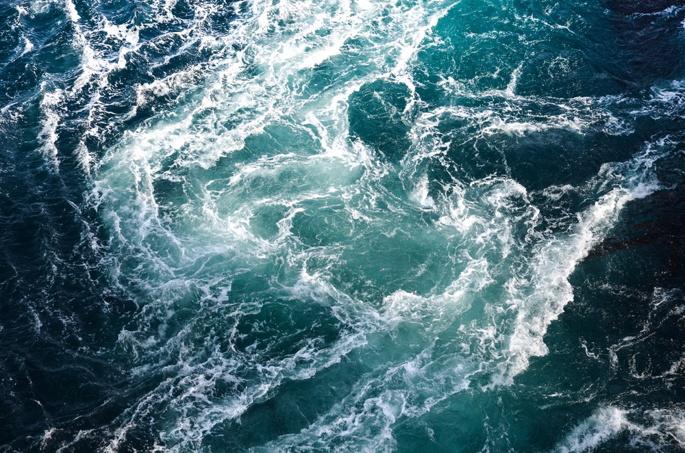 Κύματα θαλασσινού νερού συναντούν τους υποβρύχιους μυτερούς βράχους και δημιουργούν δίνες.