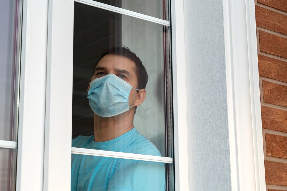 Αυτοαπομόνωση σε καραντίνα. Άνθρωπος με ιατρική μάσκα στο παράθυρο.