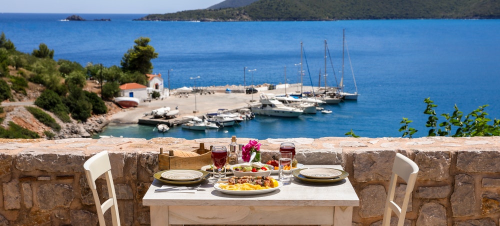 Tisch für zwei Personen mit Hähnchen-Souvlaki und Pommes frites, griechischem Salat, Snacks und Getränken auf der Sommerterrasse