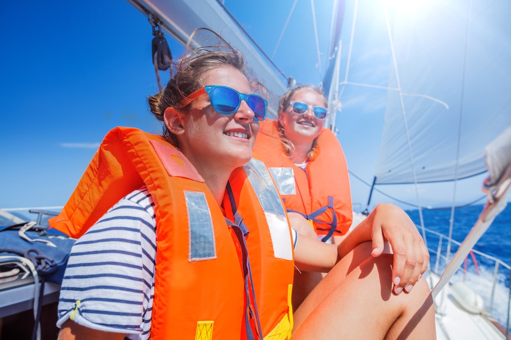 Dievčatá na palube plachetnice so záchrannou vestou a slnečnými okuliarmi.