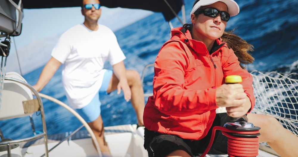 Donna in abbigliamento sportivo e occhiali da sole a bordo di una barca a vela
