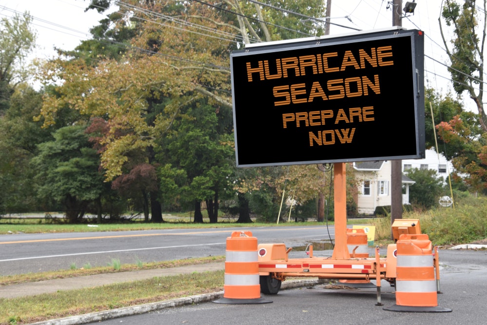 Ein digitales, elektronisches, mobiles Straßenschild mit der Aufschrift "Get Ready for Hurricane Season" (Machen Sie sich bereit für die Hurrikan-Saison), das an einer von Bäumen gesäumten Straße in der Nachbarschaft angebracht ist.