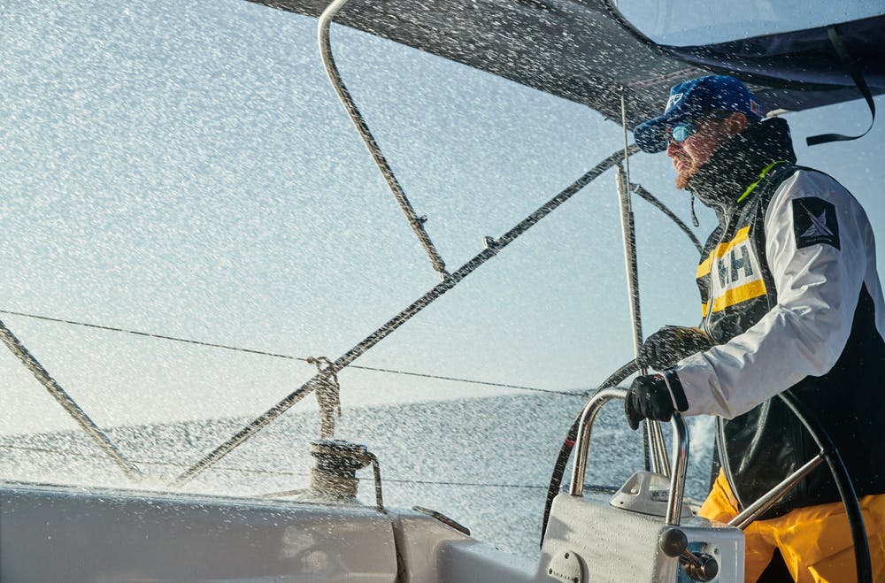 Spain, Malorca, 29 April 2018: The brutal man at yacht steering wheel during a storm, splashes fly to a face, the person is dressed in waterproof clothes and sunglasses