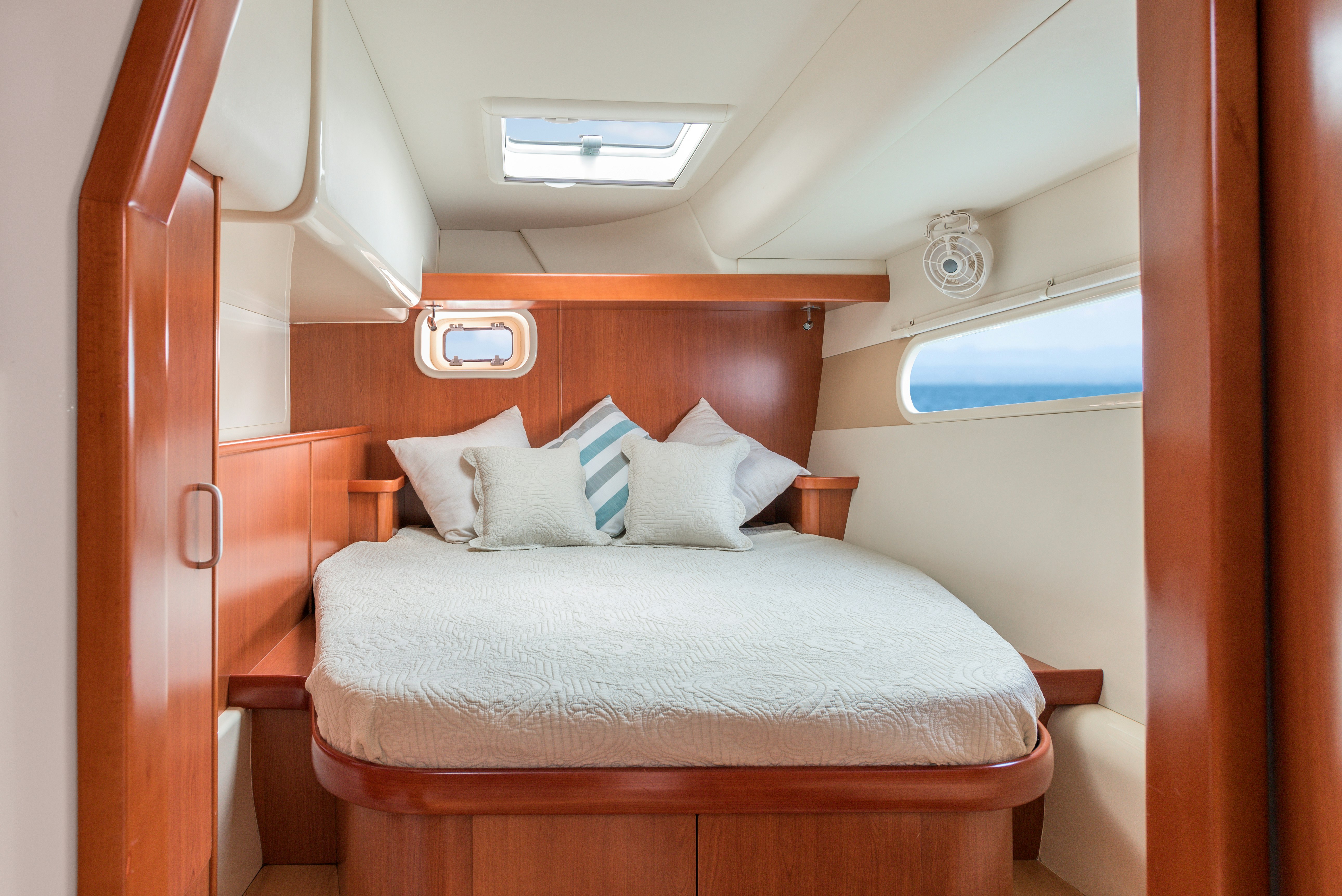 Sleeping bedroomberth on private sailing catamaran with white and blue cushions, white bedding and with Mediterranean sea view through the port light