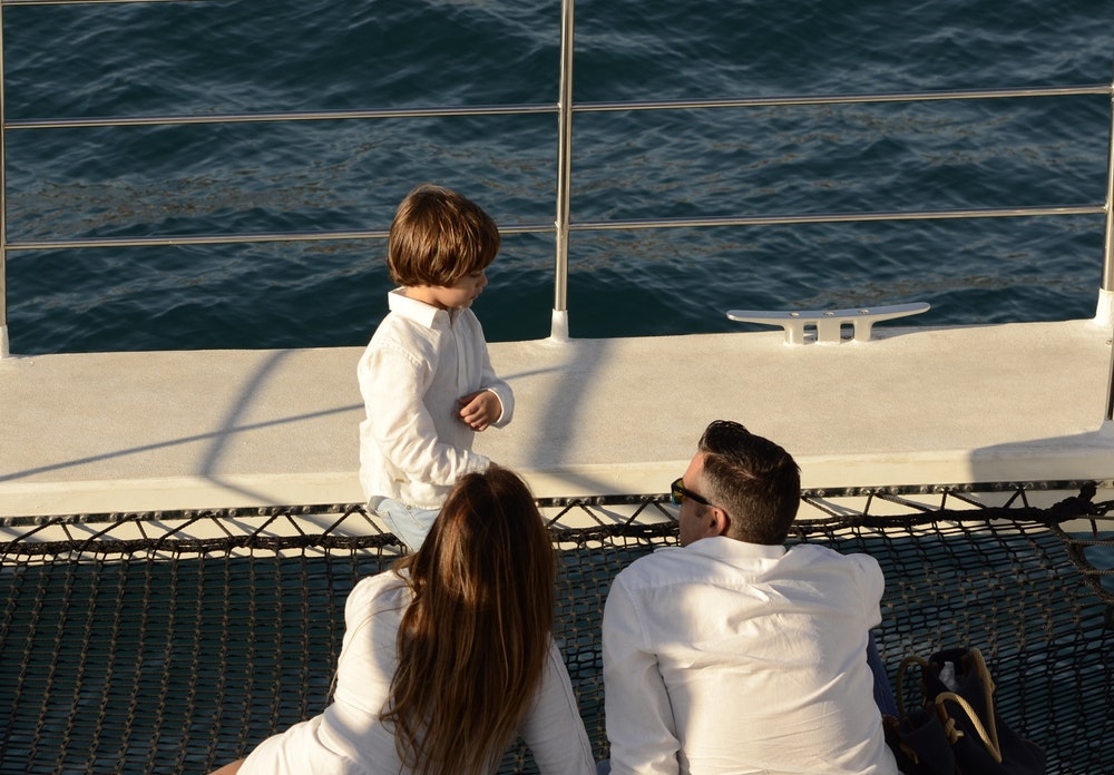 Mamma, papà e figlio sdraiati sulla rete di un grande catamarano.