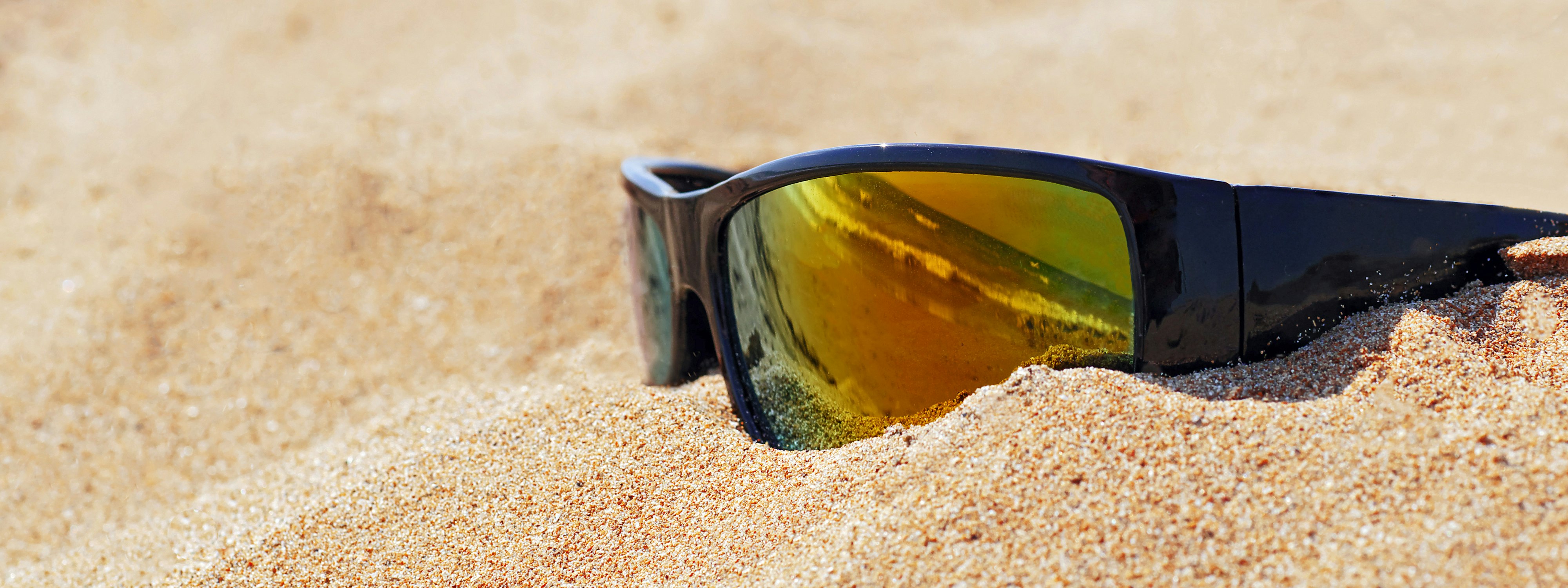 closeup of mirror sunglasses on sand on beach reflecting sea waves, suitable for header or banner