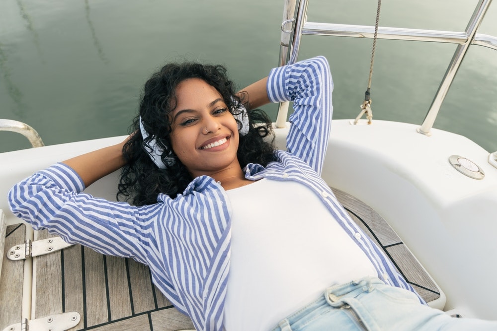 Cheerful ethnic woman listening to music on yacht