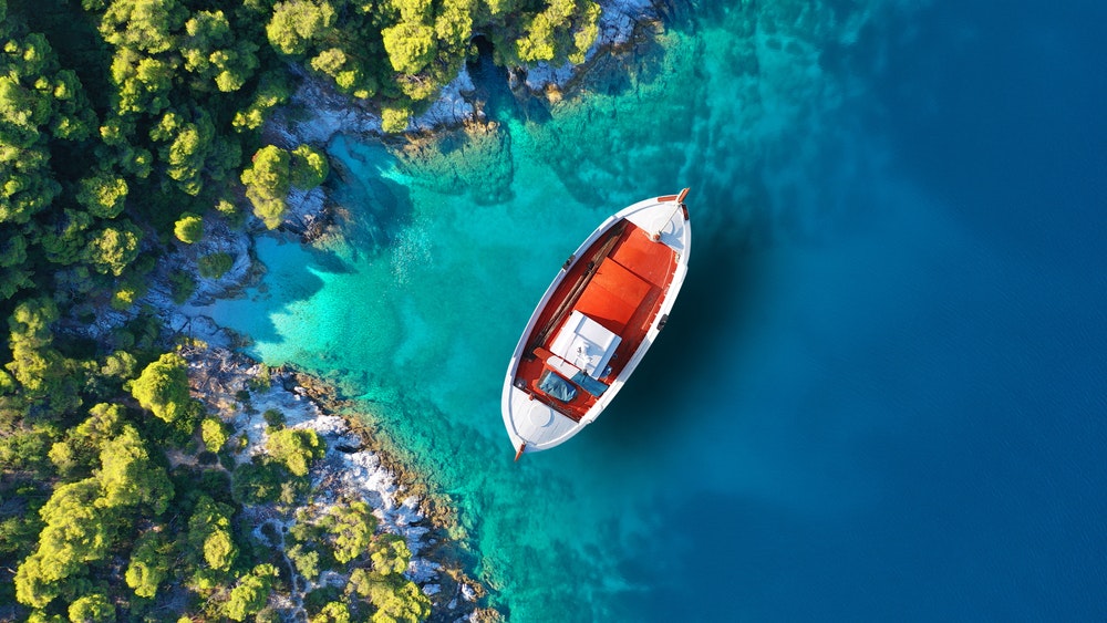 Foto aerea di una barca da pesca tradizionale ormeggiata vicino al piccolo e pittoresco porto di Agnontas, Skopelos, Sporadi