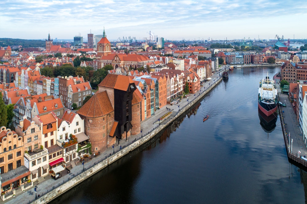 De oude stad Gdansk in Polen met de oudste middeleeuwse havenkraan (Zuraw) van Europa, de St. John's kerk, de Motlawa rivier, oude graanschuren, schepen en een boot.