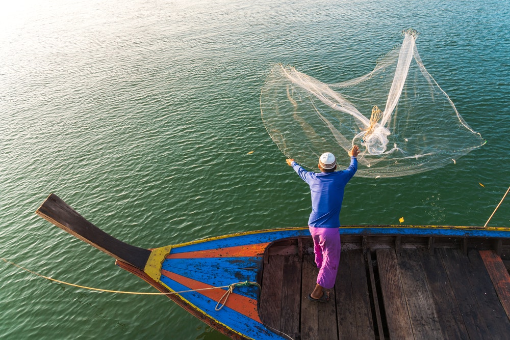Un pescatore in Thailandia getta in acqua una rete da pesca
